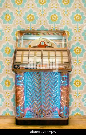 Bunte Vintage Jukebox vor Retro-Blumen-Tapete auf einem Holzboden Stockfoto