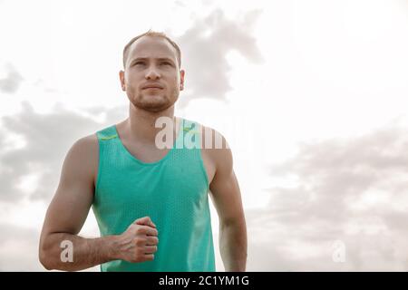 Portrait der kaukasischen Kerl in einem Azure T-Shirt und schwarze Shorts über unebenes Gelände laufen. Ausbildung bei Sonnenuntergang Stockfoto