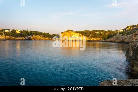 Sonnenaufgang auf felsiger Spitze mit privaten Villen über dem ruhigen azurblauen Meer auf der Baleareninsel. Bucht mit türkisblauem Wasser auf Mallorca, Spanien. Stockfoto