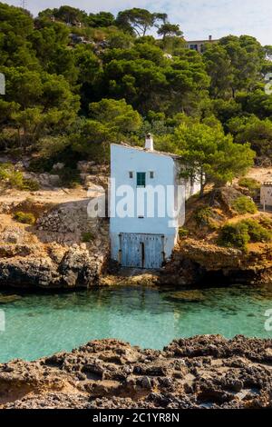 Schöne Aussicht Felsen Bucht Strand traditionelles Haus Dorf, Cala S'Almunia, Mallorca Insel, Spanien. Private Villen über ruhigen azurblauen Meer während Sonnenaufgang Stockfoto