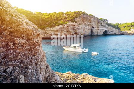 Kleine Yacht schwimmt in klarem azurblaues Meer während Sonnenuntergang, Mallorca, Spanien. Boot in der Nähe im Mittelmeer verankert. Tolle Bucht mit Ruhe Stockfoto