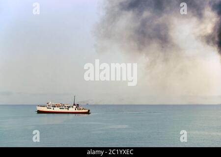 Auspuffrohr des Fährschiffs mit schwarzem dichtem Rauch, der herauskommt, und Himmel mit Wolken auf dem Hintergrund. Luftverschmutzung. Stockfoto