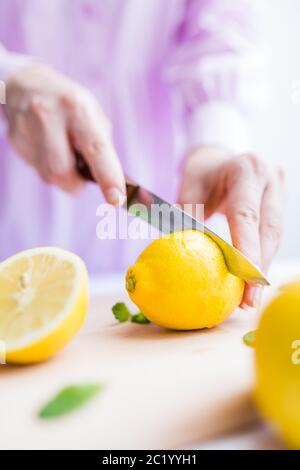 Nahaufnahme der Frau Schneiden frische Zitrone auf Holzbrett am Tisch. Stockfoto