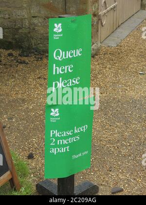 Der National Trust verwendet grüne Schilder, um zu empfehlen, 2 m auseinander zu halten und 'Bitte hier anstehen'. Stockfoto
