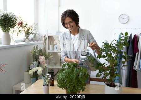 Lächelnde junge Frau Wasser grünen Pflanzen im Büro Stockfoto