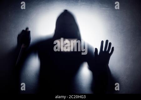 Mann in einer Haube und weiße Maske mit Messer hinter einer staubigen zerkratzt Glas Stockfoto