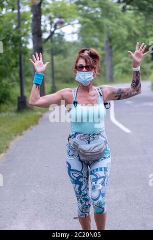 Eine attraktive Frau mittleren Alters läuft auf dem Weg in der Nähe der Bayside Marina, während sie eine Maske über dem Mund trägt. In Bayside, Queens, New York.Wears, Stockfoto