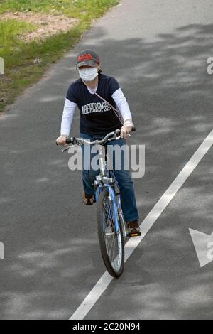 Eine junge Dame, die mit einer OP-Maske und Schutzhandschuhen unterwegs ist. Auf einem Radweg in der Nähe der Bayside Marina in Queens, New York. Stockfoto