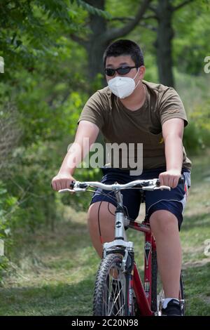 Ein junger Mann aus Asien, wahrscheinlich Koreaner, radelt auf einem Pfad nahe dem Cross Island Parkway mit einer OP-Maske. In Bayside, Queens, NYC. Stockfoto