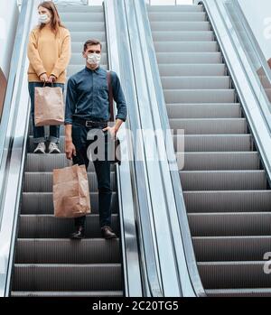 Junger Mann in einer Schutzmaske, der auf einer Rolltreppe in einem Einkaufszentrum steht Stockfoto