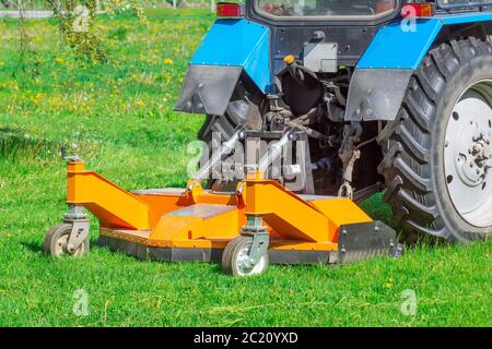 Traktor verwendet gezogene Rasenmäher, um Gras auf Stadtrasen zu mähen, Rückansicht Stockfoto