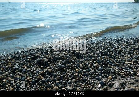 Kiesstrand mit leichten Wellen und Reflexionen im Wasser Stockfoto