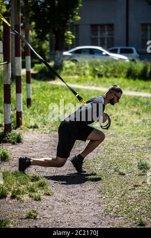 Attraktiver starker Mann macht Crossfit Liegestütze mit TRX Fitness-Gurten. Stockfoto