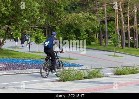 Nowosibirsk, Russland - 06.06.2020: Menschen entspannen, spazieren und verbringen ein Wochenende im Park, ein Mann fährt ein Fahrrad auf einem speziell ausgewiesenen Weg in Sportbekleidung, Stockfoto