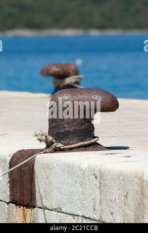 Alte und rostige Anlegestelle Poller auf Beton Pier mit blauem Meer im Hintergrund. Segeln, Urlaub, Reisen, Tourismus und maritime Aktivitäten Konzepte Stockfoto