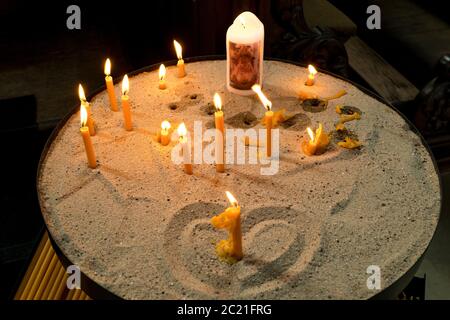 Kerzen brennen in der Kirche auf Sand mit Herz Stockfoto