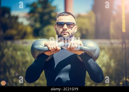 Schuss fit jungen Mann mit Kettlebell im Freien im Park trainieren. Starker junger Mann, der morgens im Park trainiert. Stockfoto