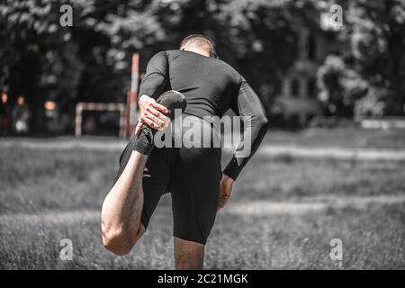 Gesunder junger Mann, der auf grünem Rasen trainiert und streckt. Meditation und Entspannung. Sport, Lifestyle und People Konzept. Stockfoto