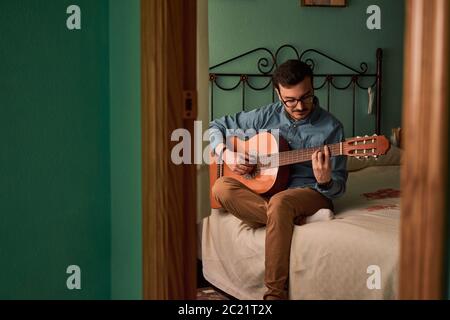 Der junge Mann spielt Gitarre in einem Raum in seinem Haus Stockfoto