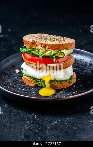 Hausgemachtes gesundes Sandwich mit Vollkornbrot, pochiertem Ei Flüssiges Eigelb, Gurke, Tomaten und Mikrokräutern Wasserkresse Salat auf dem Teller Stockfoto