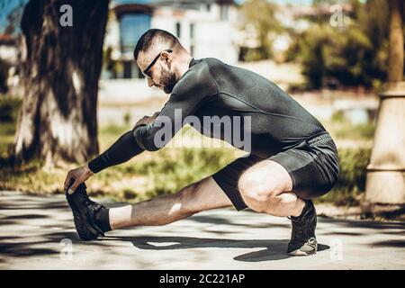 Professioneller Fitnesstrainer. Der männliche Sportler trainiert sich selbst, macht Streching. Outdoor Workout Fitness Konzept. Stockfoto