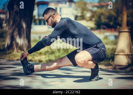 Professioneller Fitnesstrainer. Der männliche Sportler trainiert sich selbst, macht Streching. Outdoor Workout Fitness Konzept. Stockfoto