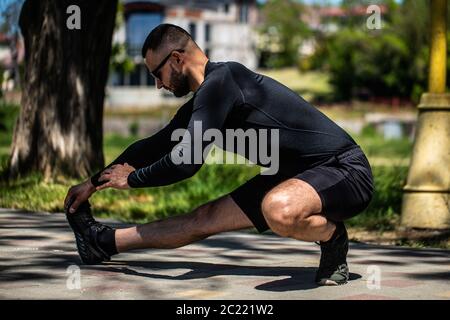 Professioneller Fitnesstrainer. Der männliche Sportler trainiert sich selbst, macht Streching. Outdoor Workout Fitness Konzept. Stockfoto