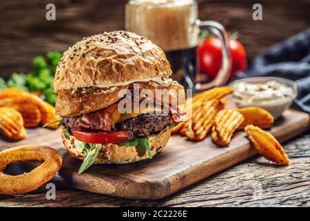 Rinderhackschnäbel mit Doppelkäse, Kartoffelkeile, Zwiebelring, Tomate, Mayonnaise und einem dunklen Bier im Hintergrund Stockfoto