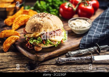 Doppelter Käseburger mit Speck und Salat in einem Sesambrötchen mit Kartoffelkeilen und Mayo auf der Seite Stockfoto