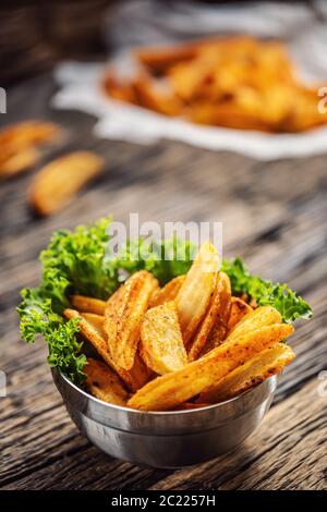 Knusprig gewürzte Kartoffelkeile in einer Metallschüssel mit Salatblatt auf dunklem Holz Stockfoto