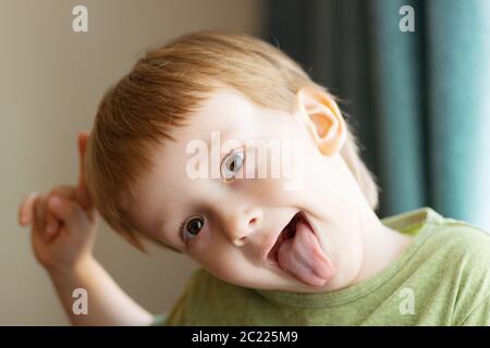 Netter Junge, der ihre Zunge zeigt. Kind legt Zunge aus - Nahaufnahme. Stockfoto