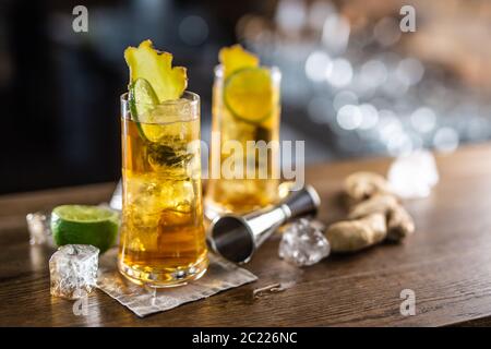Zwei Gläser Ingwer Bourbon Cocktail mit Eiswürfeln und frischem Ingwer auf einer Holzoberfläche Stockfoto