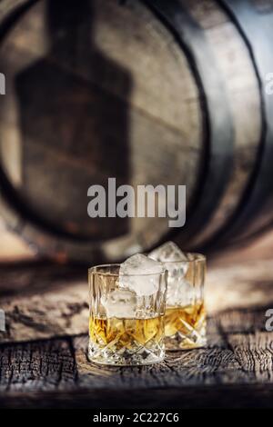 Zwei Tassen Whisky auf rustikalem Holz und ein Schatten einer Flasche, der sich auf einem Holzfass spiegelt Stockfoto