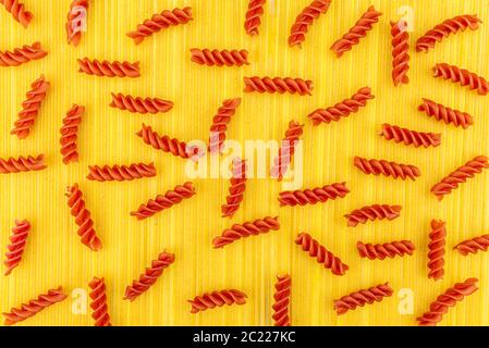 Eine rote Spirale Pasta auf gelbem Hintergrund aus langen gelben Spaghetti Pasta, Draufsicht. Stockfoto