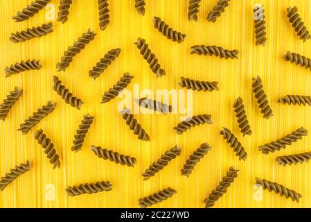 Eine dunkelgrüne Spiralnudeln auf gelbem Hintergrund aus langen gelben Spaghetti-Nudeln, Draufsicht. Stockfoto