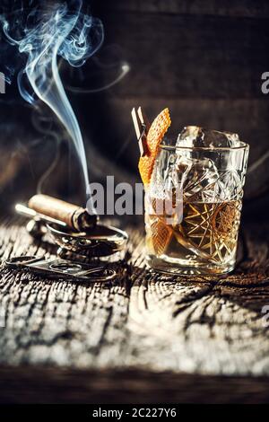 Whisky ohne Eis in einer Tasse mit brennender Zigarre und einem alten Holzfass im Hintergrund Stockfoto