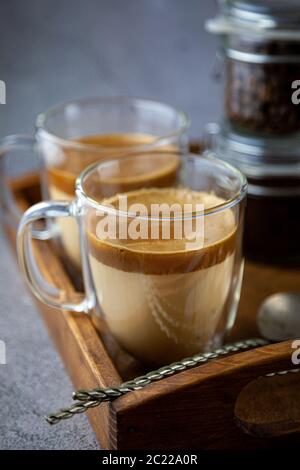 Zwei transparente Tassen mit Doppelwänden. Latte - Kaffee mit Milch auf einem Tablett. Frühstück ist auf dem Tisch. Stillleben Kaffeepause. Nahaufnahme. Stockfoto