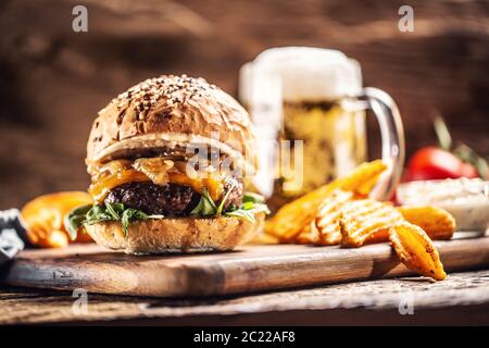 Rinderburger mit karamellisierten Zwiebeln, Rucola und geschmolzenem Käse mit Kartoffelkeilen und Fassbier im Hintergrund Stockfoto