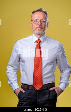 Inhalt Senior Business man in Hemd und Weste. Posiert im Studio auf gelbem Hintergrund. Selbstbewusst. Geschäftskonzept Stockfoto