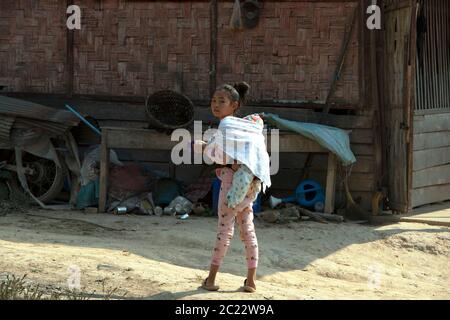 Ein junges, indigenes, ethnisches Lanten-Mädchen, das in ihrem Dorf in der Provinz Luang Namtha im Norden Laos ein Baby trägt. Stockfoto