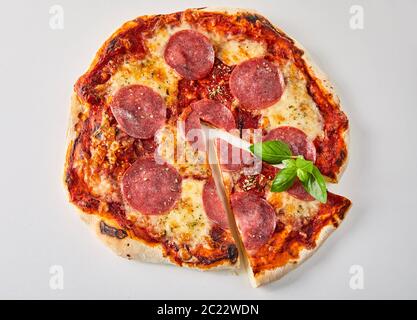 In Scheiben geschnittene Pepperoni Pizza mit frischem Basilikum Blätter, geschmolzenen Mozzarella und Tomatenmark gewürzt mit Kräutern aus gesehen oben auf weißem isoliert Stockfoto