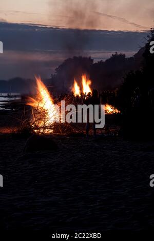 Nicht erkennbare Menschen feiern Sommersonnenwende mit großen Lagerfeuer am Strand Stockfoto