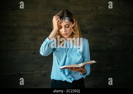 Müde, erschöpft Frau sieht, hält ein Buch, Ihr Kopf hält mit Hand, Brille auf die Stirn, überarbeitet. In Bluse angezogen. Stockfoto