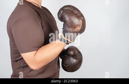 Junge Mann steht in einem Rack, das Tragen von sehr alten Vintage Brown Boxhandschuhe auf seinen Händen, weißer Hintergrund Stockfoto