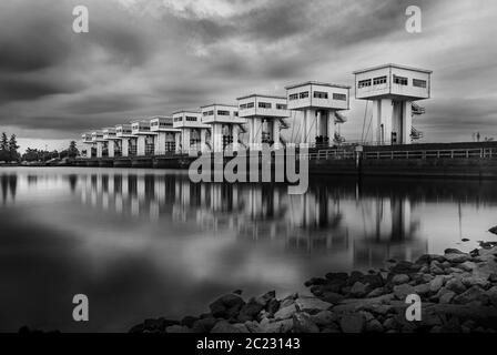 Wasserbarriere mit Wolkenhimmel bei Sonnenuntergang und Fluss-Langzeitbelichtung, Schwarz-Weiß und monochromen Stil Stockfoto