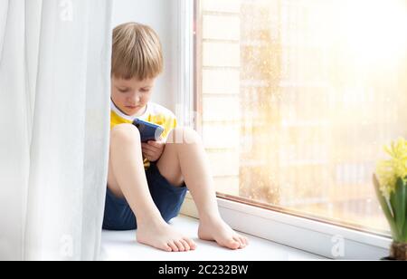 Kleines Kind mit Smartphone auf Fensterbank, Platz für Text. Konzept - Quarantäne, Gefahr des Internets Stockfoto