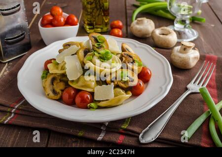 Hausgemachte Tortellini gefüllt mit Pilzen und Frühlingszwiebeln, gerösteten Tomaten, Knoblauch Souce gekrönt parmesan Stockfoto