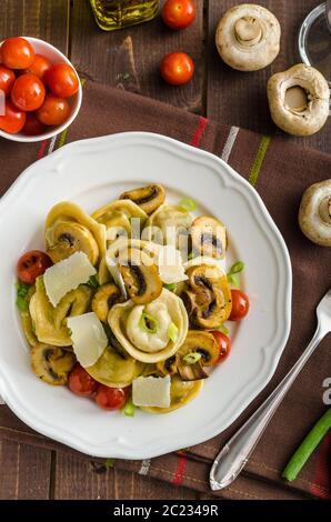 Hausgemachte Tortellini gefüllt mit Pilzen und Frühlingszwiebeln, gerösteten Tomaten, Knoblauch Souce gekrönt parmesan Stockfoto