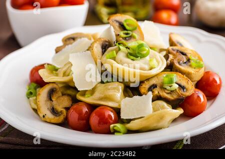 Hausgemachte Tortellini gefüllt mit Pilzen und Frühlingszwiebeln, gerösteten Tomaten, Knoblauch Souce gekrönt parmesan Stockfoto