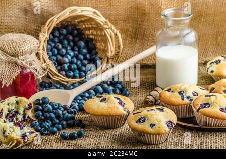 Blueberry Muffins Milch und Marmelade im Hintergrund und Korb voll mit Heidelbeeren Stockfoto